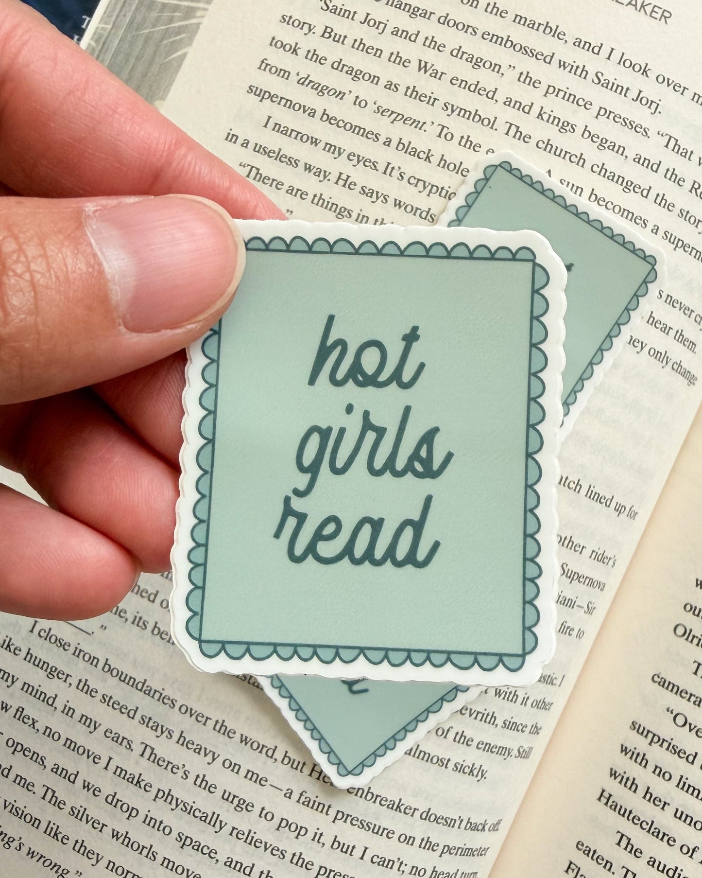 Hand holding a 'hot girls read' sticker over an open book