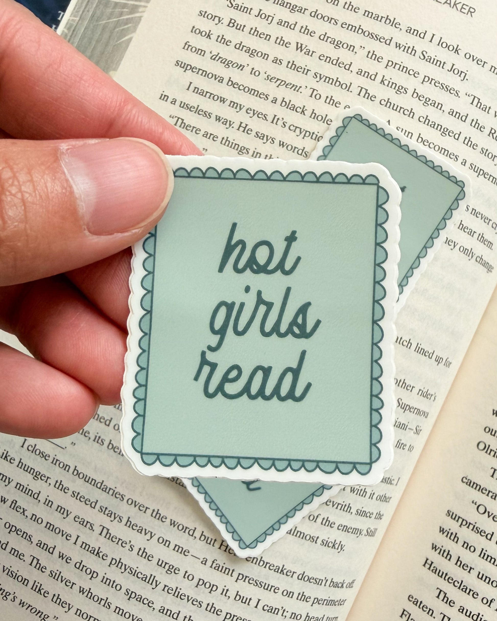 Hand holding a 'hot girls read' sticker over an open book