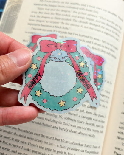 Hand holding a decorative sticker with a wreath design over an open book