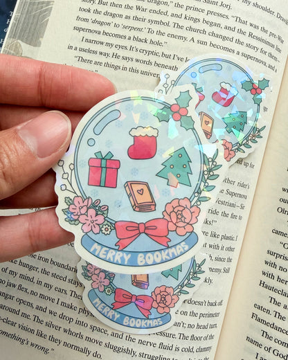 Decorative sticker with 'Merry Bookmas' text held over an open book.