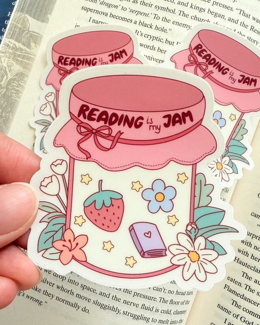 Sticker with 'Reading is my Jam' design held over an open book