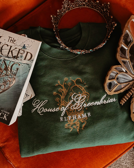 Green shirt with 'House of Greenbar' design, book, and decorative items on an orange surface