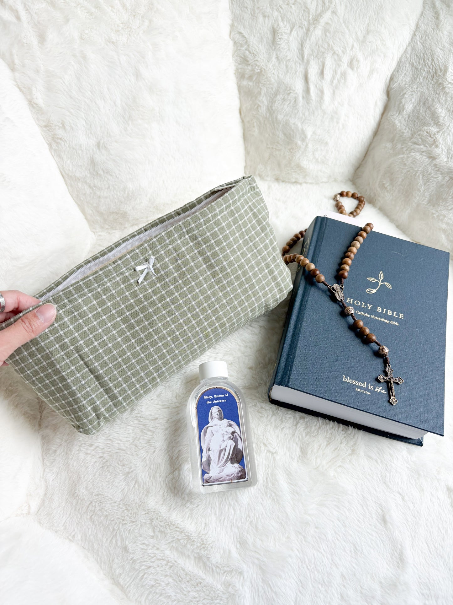 Dusty pink quilted pouch open with contents including rosary, perfume, earbuds, and scrunchie