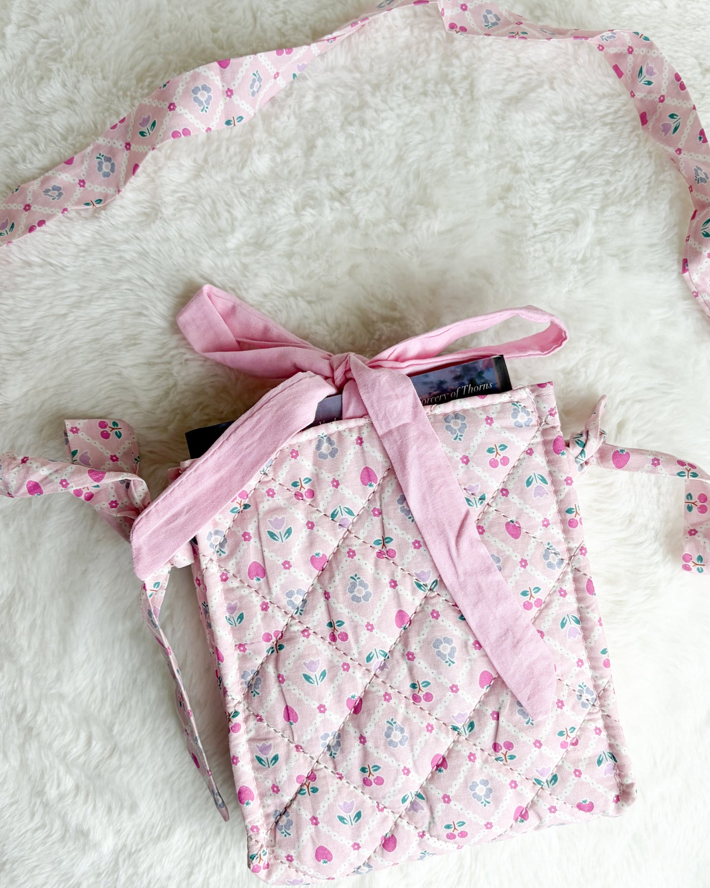 A small quilted fabric bag in a pink floral print with a matching pink ribbon bow, laid on a white faux fur surface.