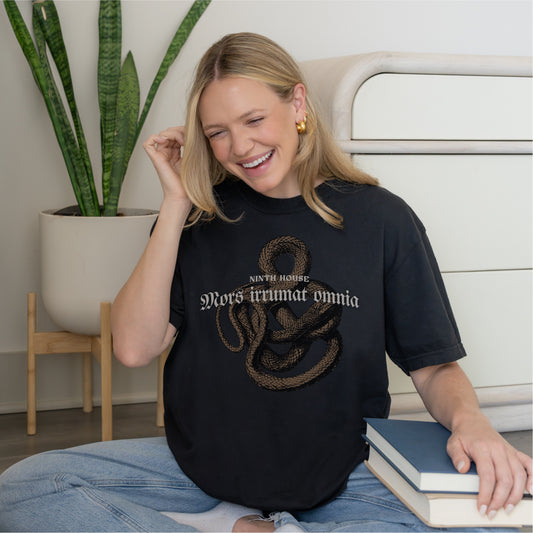 Smiling woman in black Ninth House t-shirt with snake graphic and Latin text, holding books