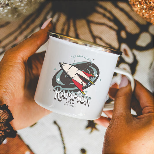 White enamel mug featuring illustrated spaceship, Rampion Crew design, held in hands
