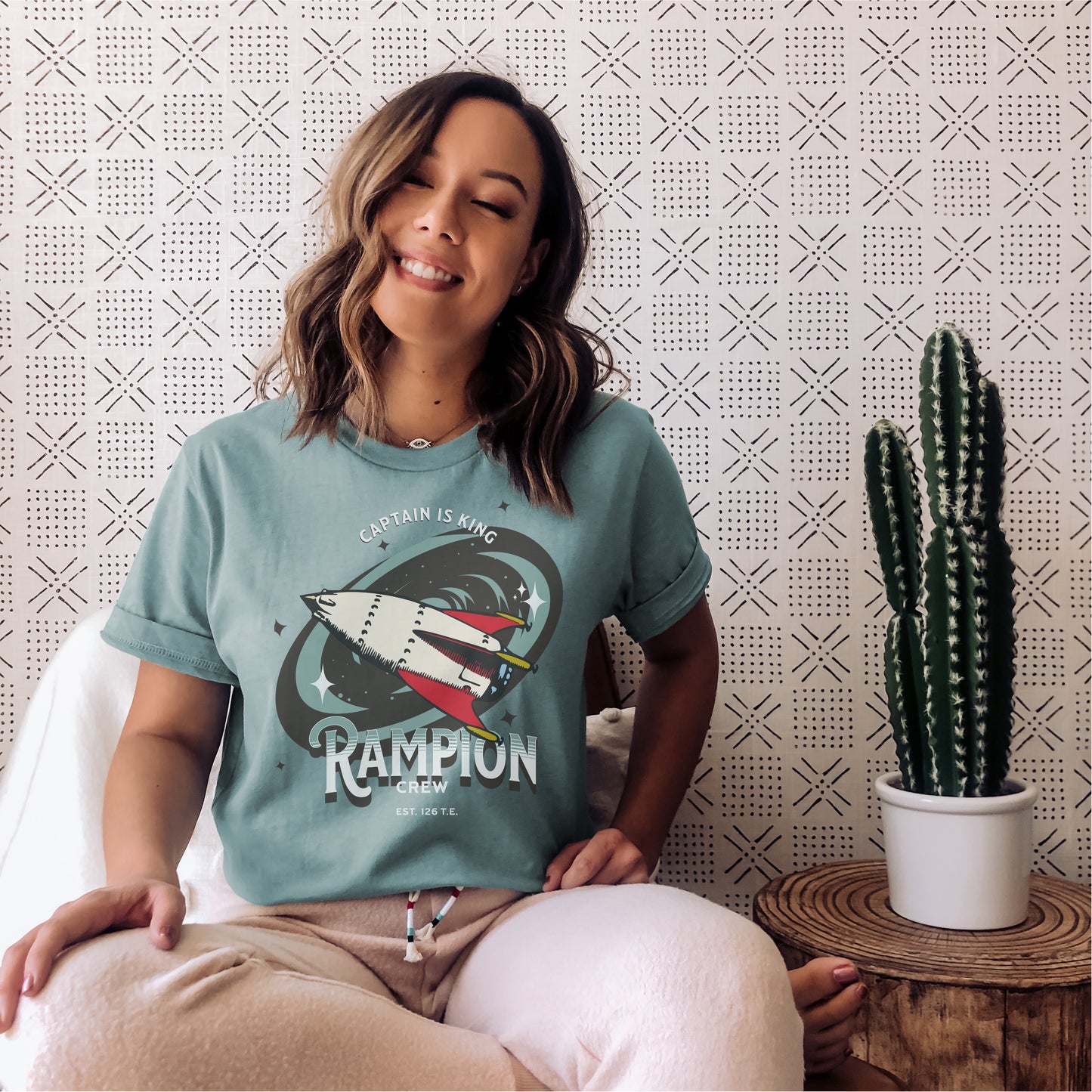 Woman wearing Rampion Crew t-shirt with spaceship graphic, sitting indoors near cactus