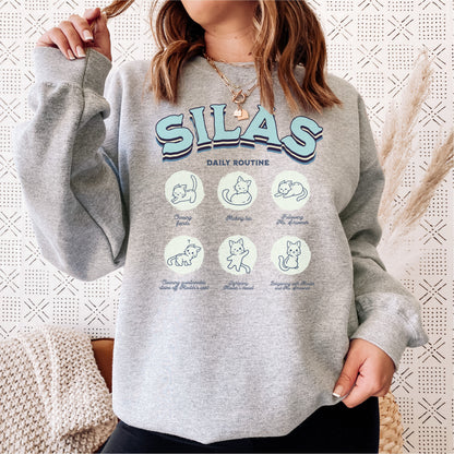 Woman wearing grey Silas sweatshirt with cute illustrated cat daily routine graphic