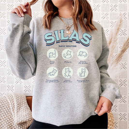 Woman wearing grey Silas sweatshirt with cute illustrated cat daily routine graphic