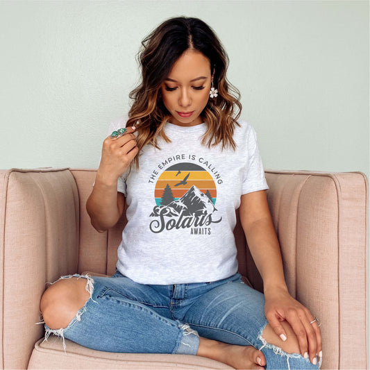 Woman wearing Solaris Awaits bookish t-shirt with mountain graphic, sitting on a sofa.