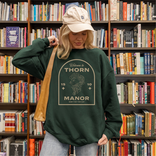 Woman in bookstore wearing dark green Thorn Manor sweatshirt with graphic and text design.