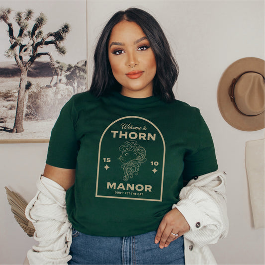 Woman wearing a green Thorn Manor graphic tee shirt with vintage-inspired bookish design