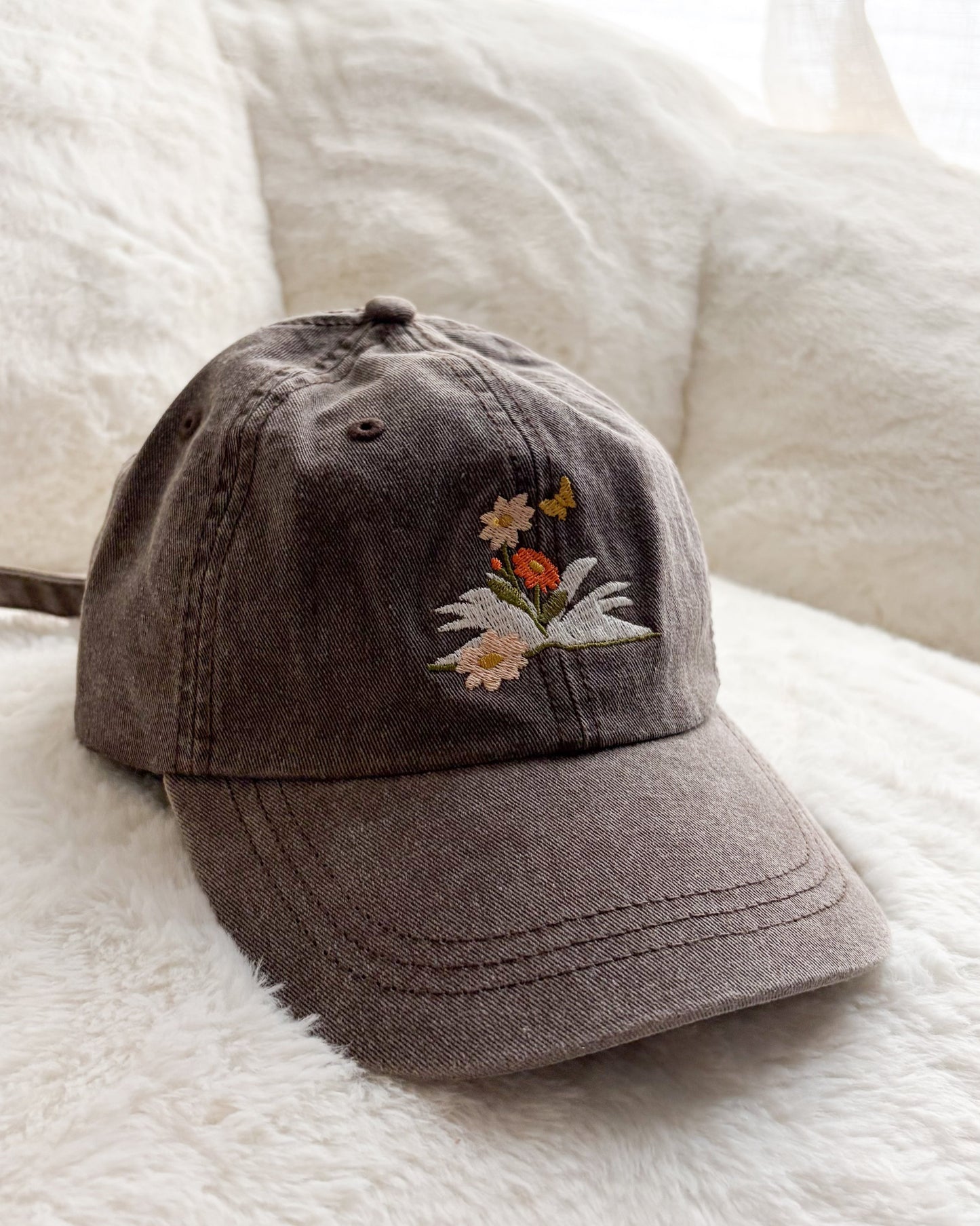Brown embroidered baseball cap with floral and butterfly design on soft white blanket
