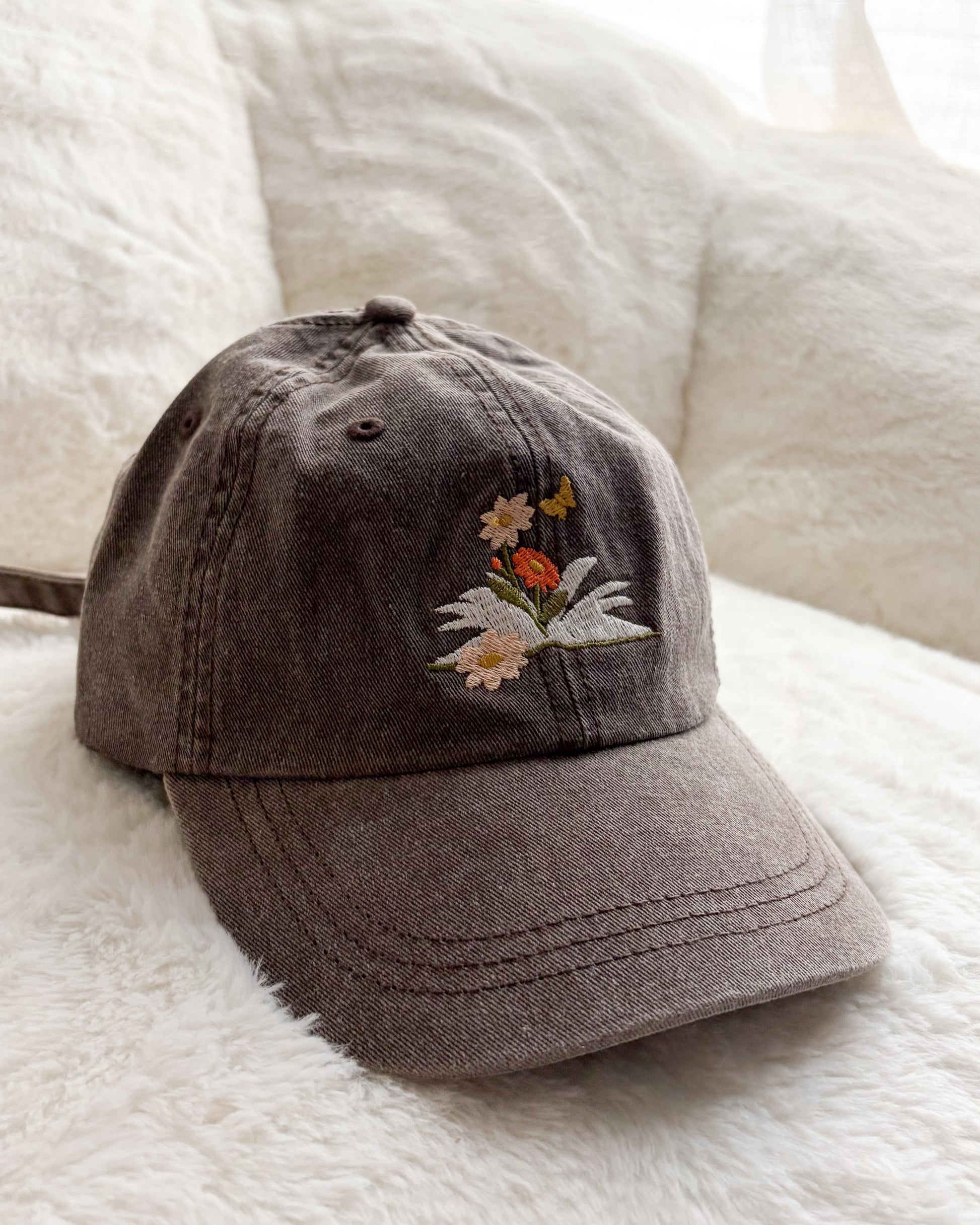 Brown embroidered baseball cap with floral and butterfly design on soft white blanket