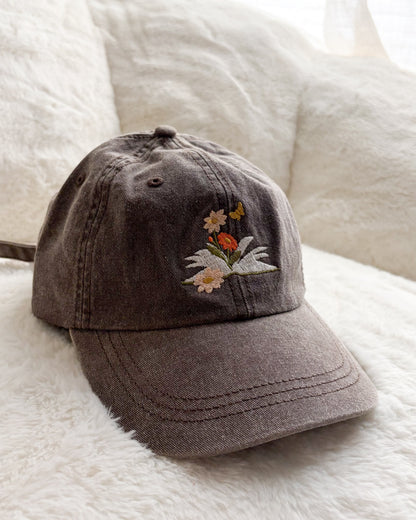 Brown embroidered baseball cap with floral and butterfly design on soft white blanket