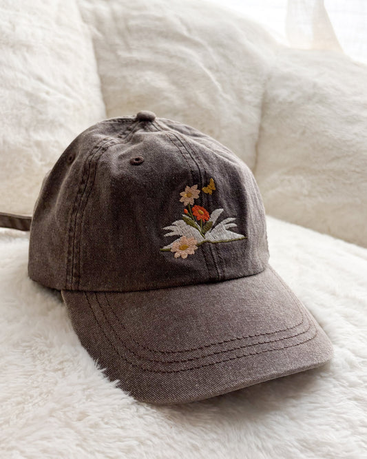 Brown embroidered baseball cap with floral and butterfly design on soft white blanket