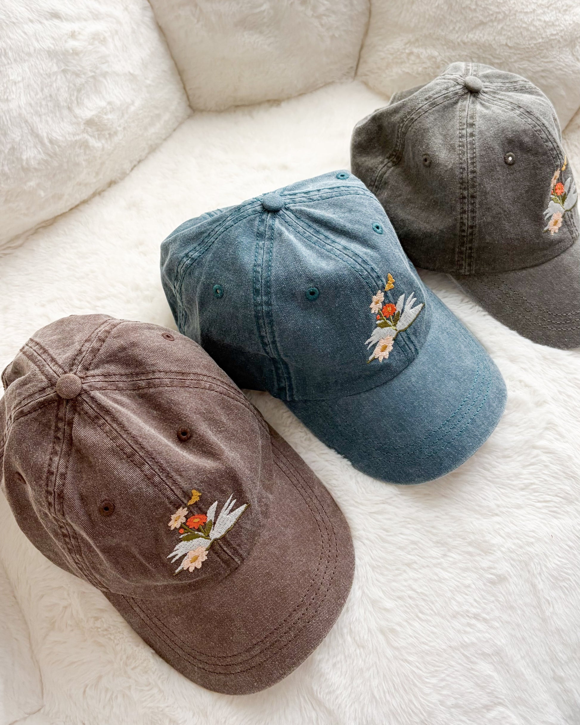 Three vintage-wash baseball caps with embroidered floral design on soft white blanket