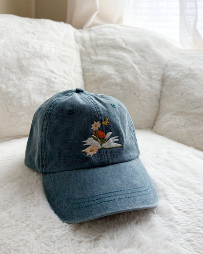 Blue denim cap with embroidered flowers and butterfly on a white plush surface