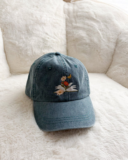 Blue denim cap with embroidered flowers and butterfly on a white plush background