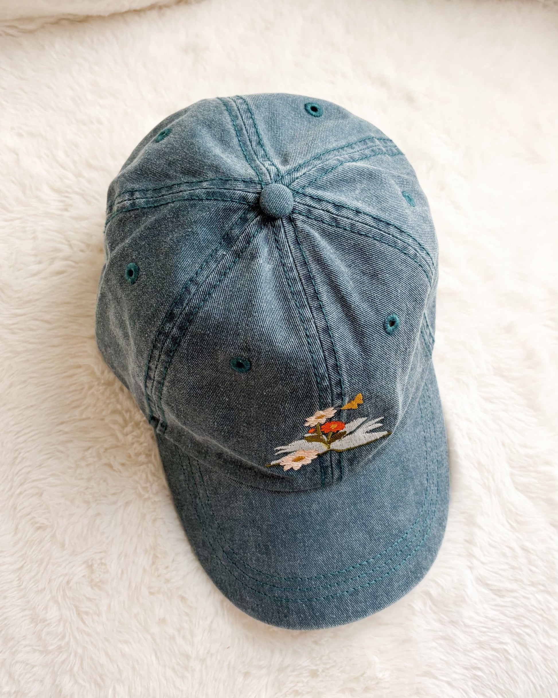 Denim baseball cap with embroidered wildflowers on soft white fabric background