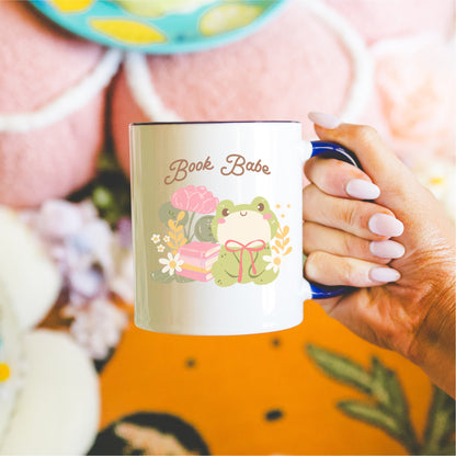 Book Babe mug with cute frog, flowers, and books illustration held in hand