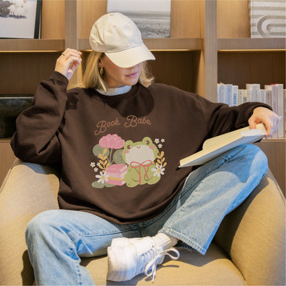Woman reading in armchair wearing brown Book Babe sweatshirt with cute frog and floral design