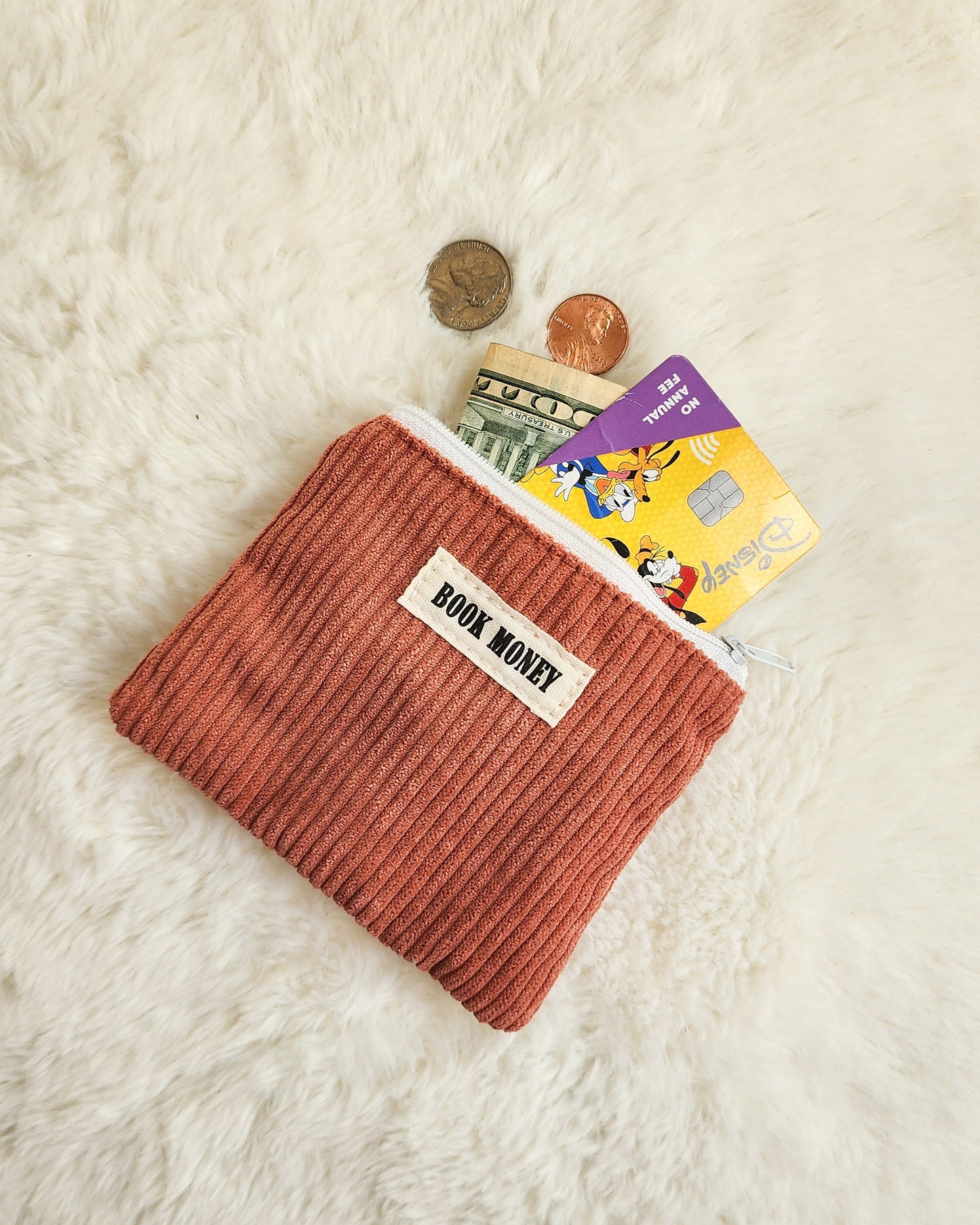 Corduroy zippered coin purse with 'Book Money' label, holding cash, coins, and cards on a white surface