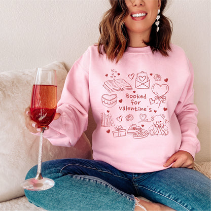 Woman wearing pink Booked for Valentine's sweatshirt with bookish designs, holding a drink