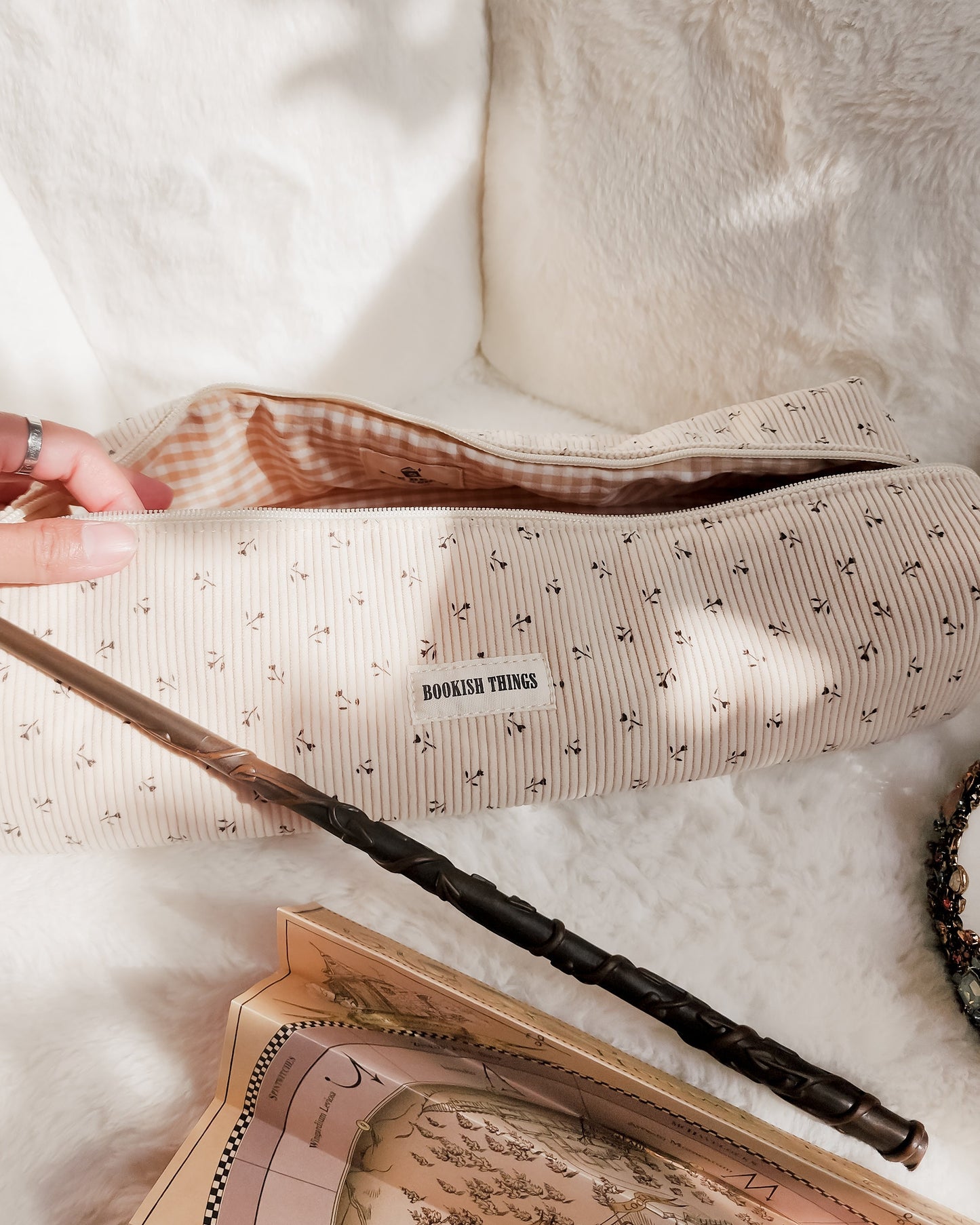 Striped corduroy travel bag with 'Bookish Things' label, magic wand, and parchment map