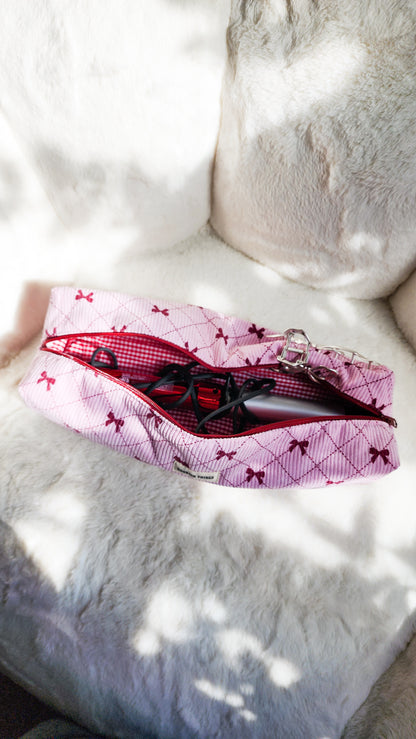 Pink corduroy travel bag with red bows holding hair styling tools on a soft white surface