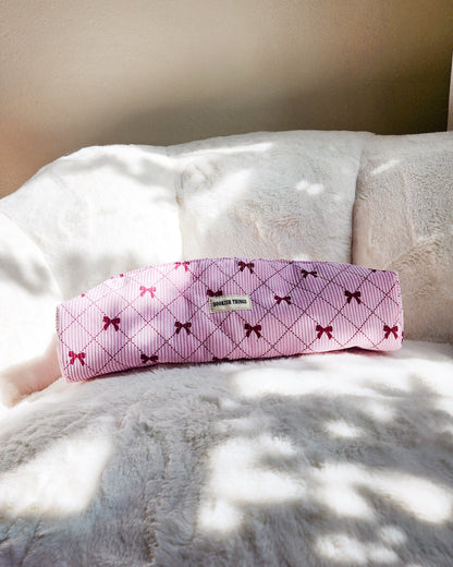 Pink corduroy travel bag with red bows and 'Bookish Things' label on a white plush blanket