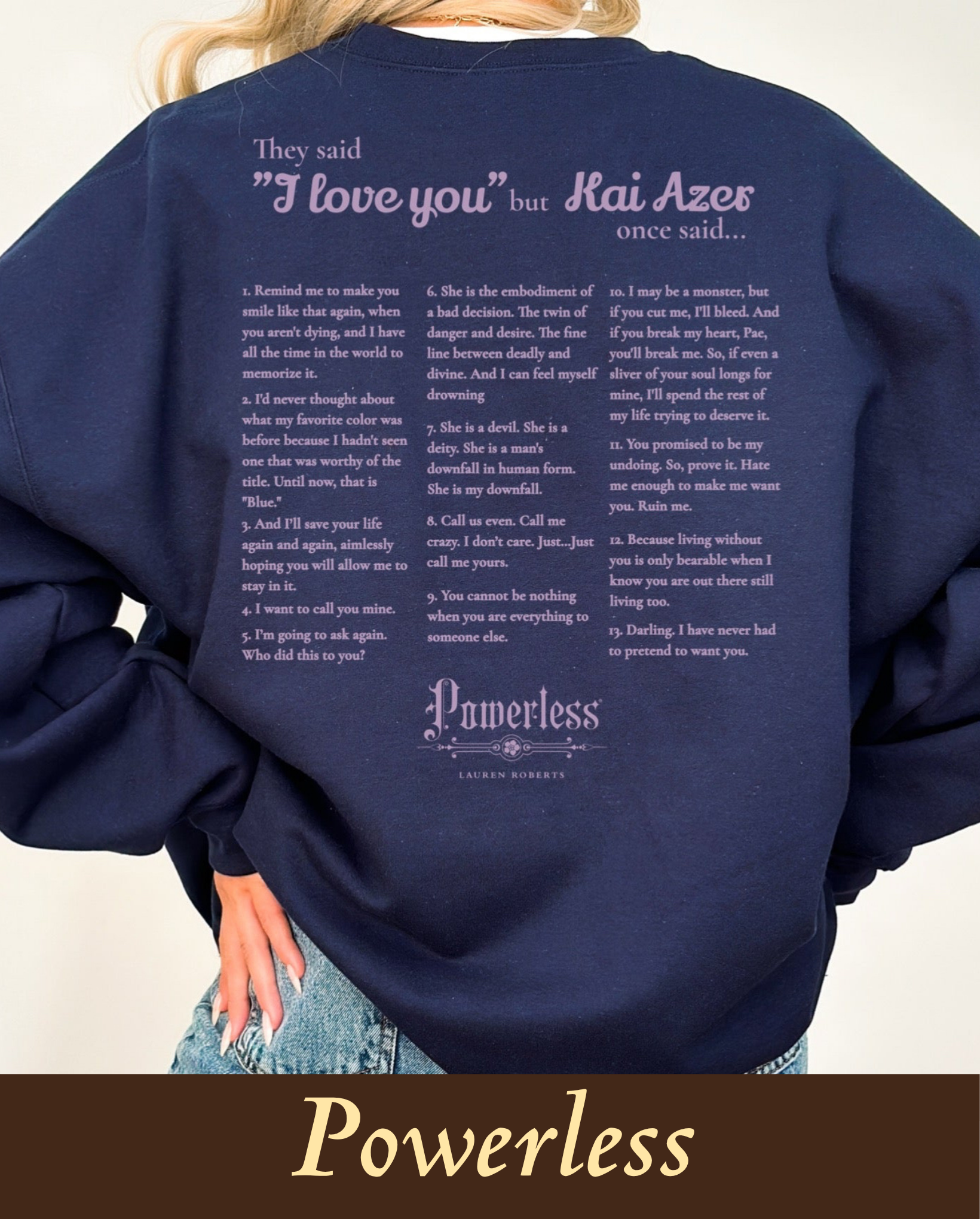 A model wearing a cozy navy blue crewneck sweatshirt featuring a detailed back print dedicated to Lauren Roberts' fantasy novel Powerless. The text reads: 'They said I love you but Kai Azer once said...' followed by a numbered list of 13 iconic romantic and moody quotes from the book character, finished with an elegant Powerless logo script at the bottom.