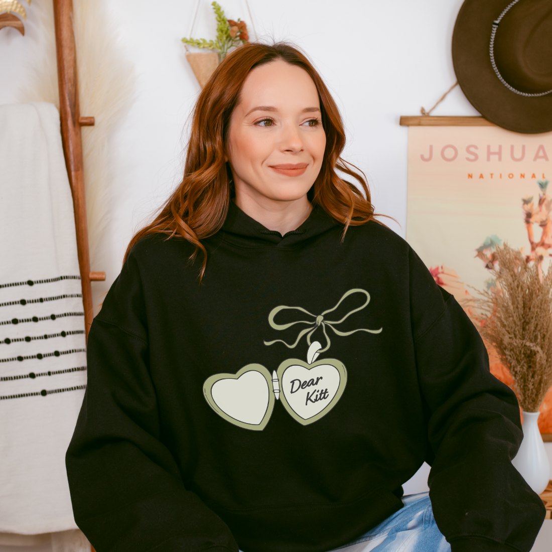Woman wearing black hoodie with heart locket graphic and 'Dear Kitt' text, cozy bookish apparel