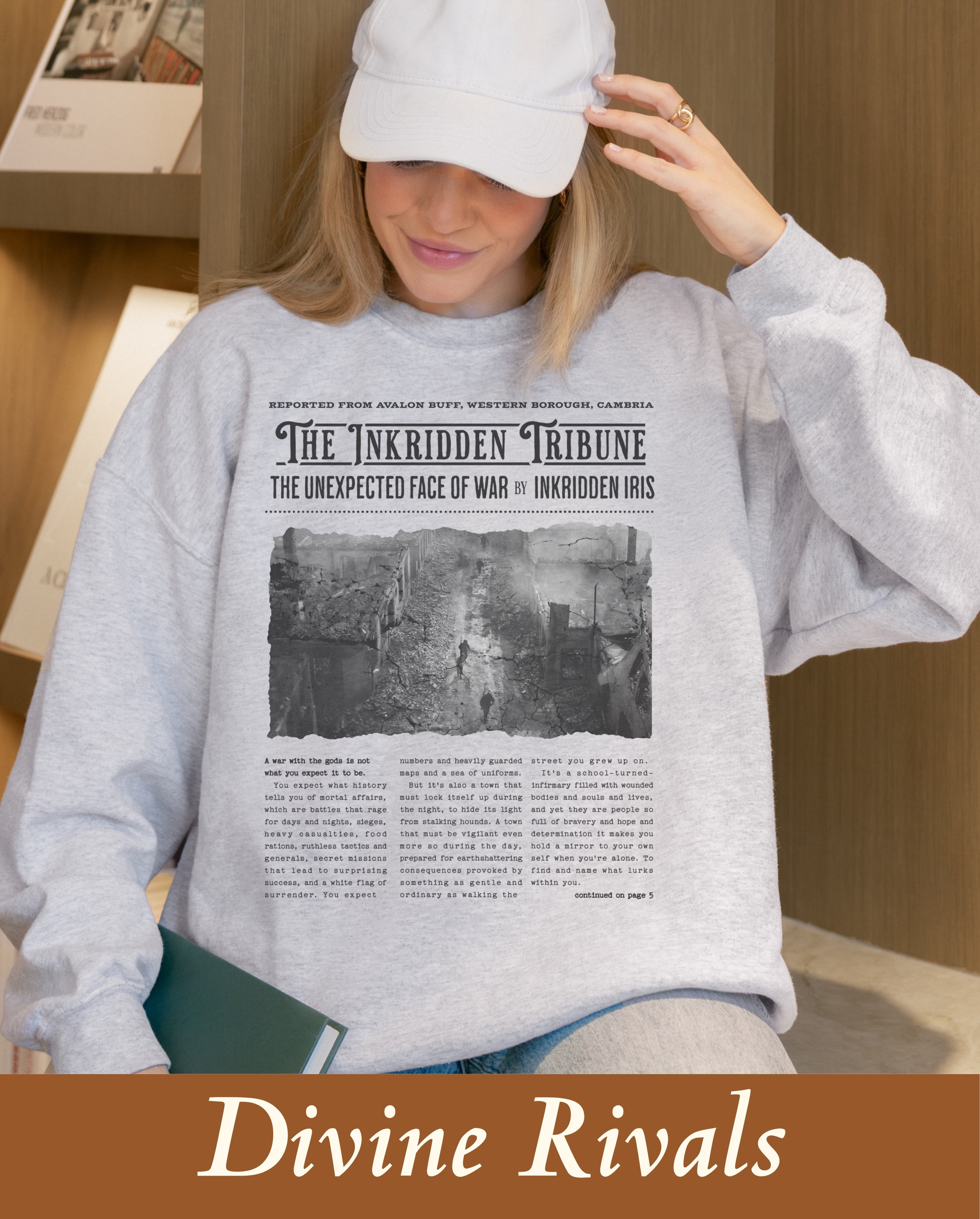 An officially licensed Divine Rivals bookish merchandise sweatshirt designed to look like a vintage fantasy newspaper, styled naturally as a comfortable and wholesome campus reading uniform outfit.