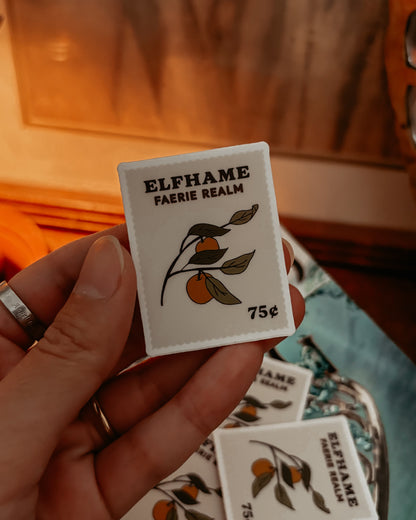 Hand holding a small patch with 'Elfhame Faerie Realm' branding and orange design.