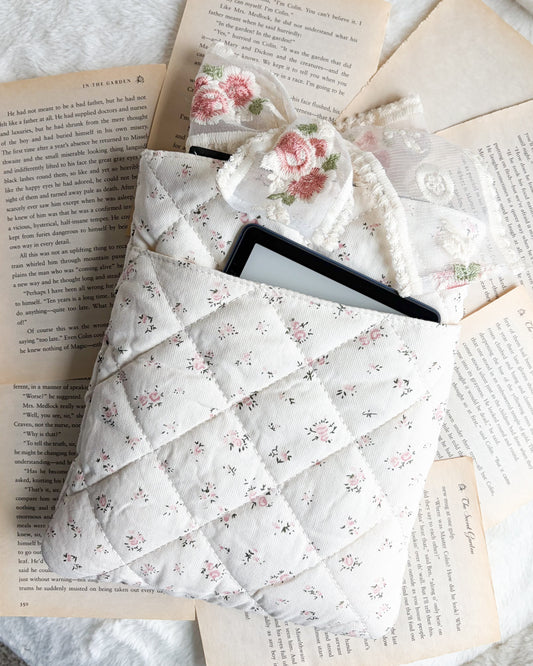 Floral quilted book sleeve with lace bow holding e-reader, styled on open book pages.