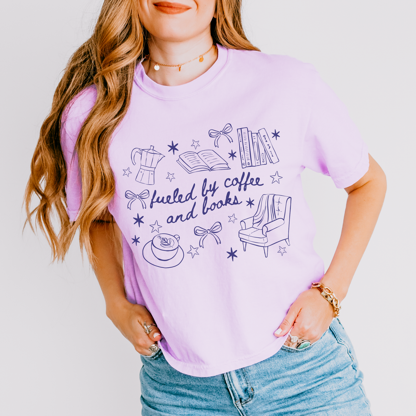 Lavender boxy tee with doodles of coffee, books, and cozy reading chair, says 'fueled by coffee and books'