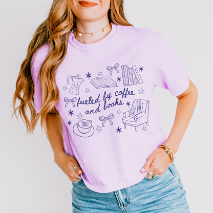 Lavender boxy tee with doodles of coffee, books, and cozy reading chair, says 'fueled by coffee and books'