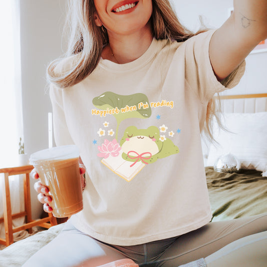 Woman wearing a cute frog reading shirt with 'Happiest when I'm reading' text, holding iced coffee