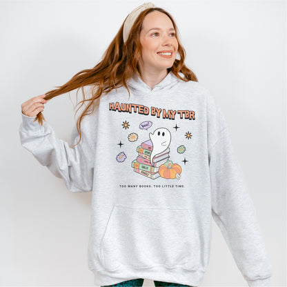Woman wearing grey hoodie with ghost, books, and 'Haunted By My TBR' bookish graphic