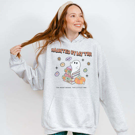 Woman wearing grey hoodie with ghost, books, and 'Haunted By My TBR' bookish graphic
