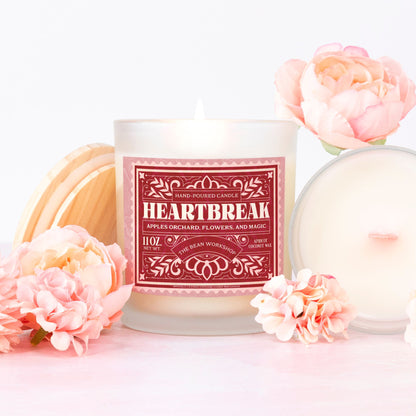 Heartbreak frosted glass candle with pink wood wick, surrounded by pink flowers