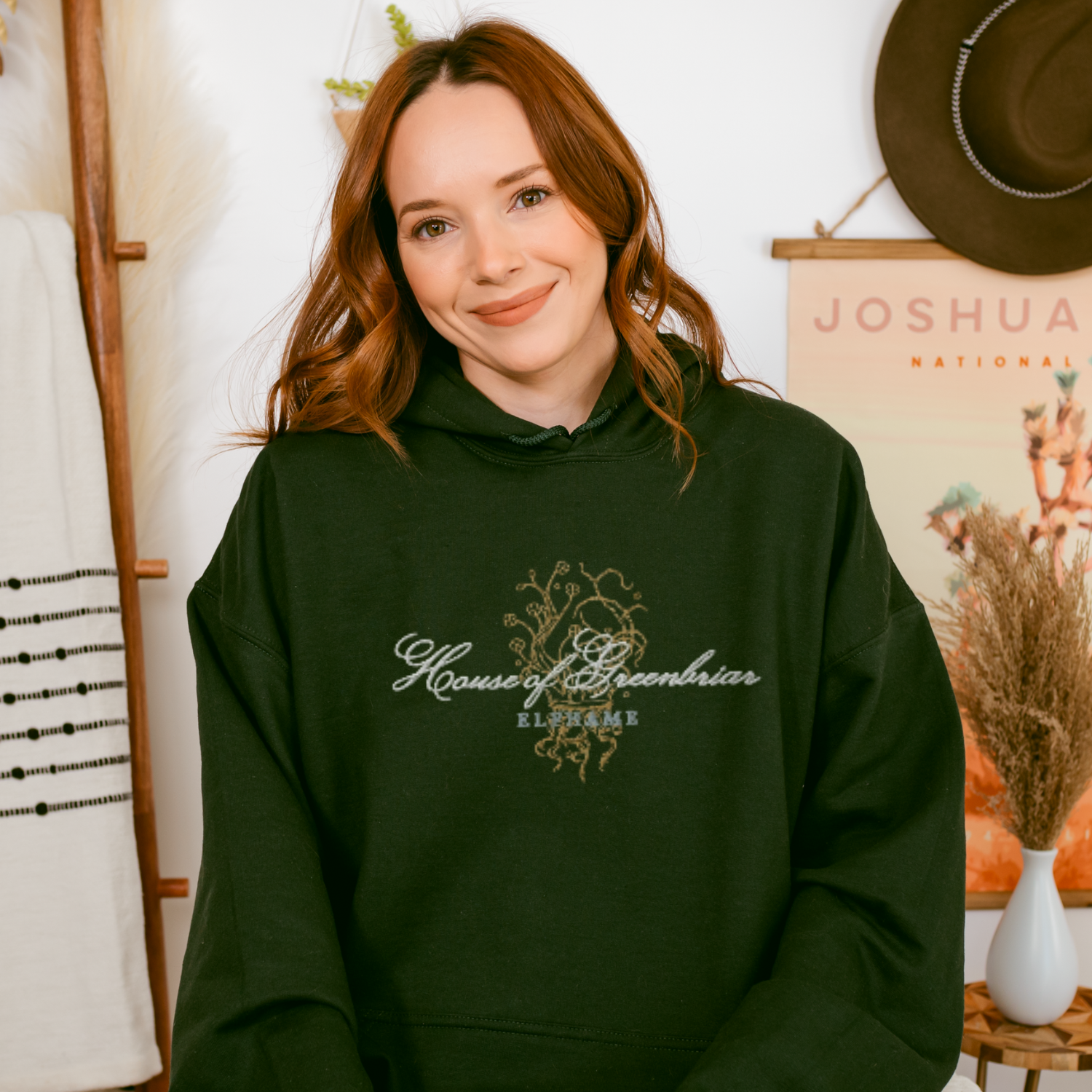 Woman wearing dark green House of Greenbriar Elfhame embroidered hoodie, bookish fashion