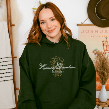 Woman wearing dark green House of Greenbriar Elfhame embroidered hoodie, bookish fashion