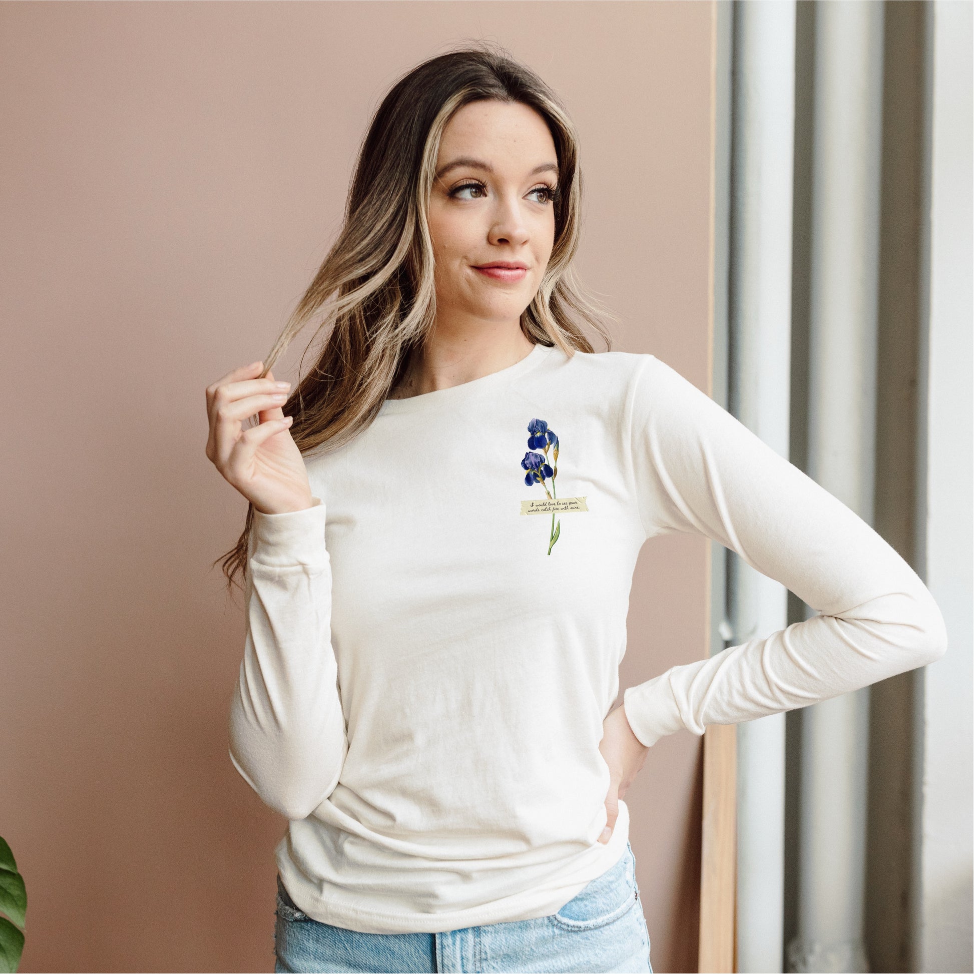 Woman wearing a cream long sleeve tee with blue flower and book quote graphic on chest