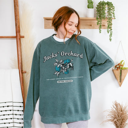 Woman wearing green Jacks' Orchard sweatshirt with apple graphic in cozy indoor setting
