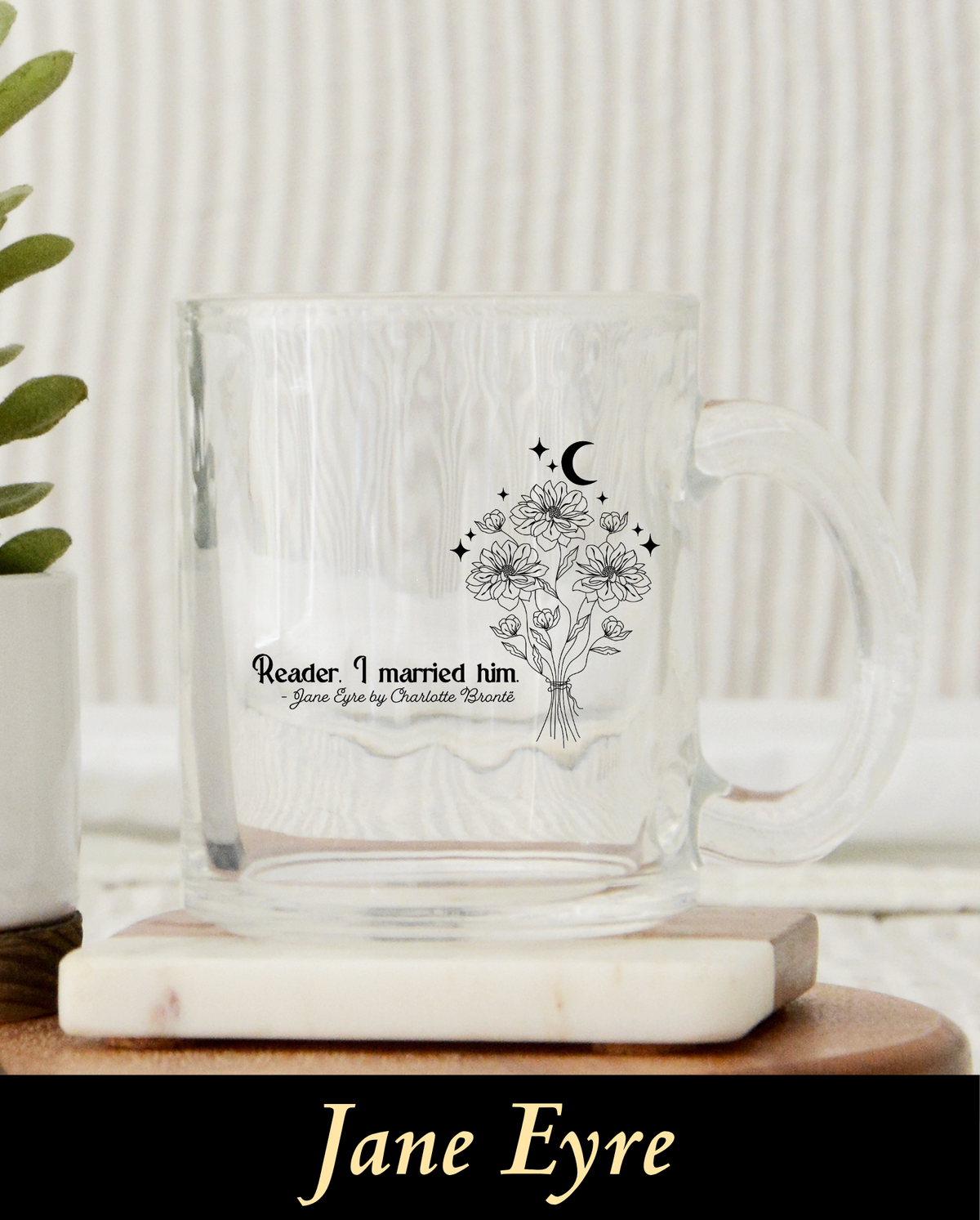 A clear glass mug featuring a delicate black line art bouquet of wild flowers beneath a celestial crescent moon and stars. Below the illustration, the famous quote reads: Reader. I married him. - Jane Eyre by Charlotte Brontë.