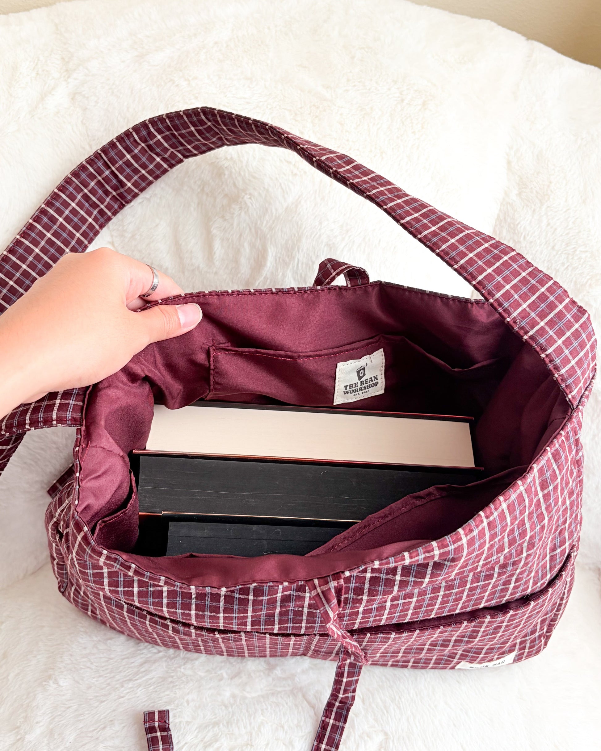 Maroon gingham book tote bag with multiple pockets holding books on white fabric
