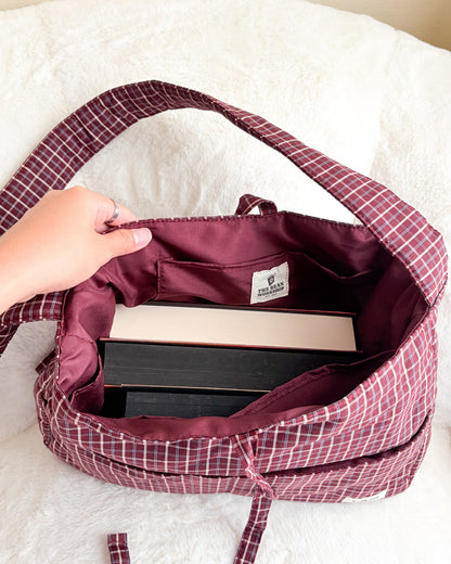 Maroon gingham book tote bag with multiple pockets holding books on white fabric
