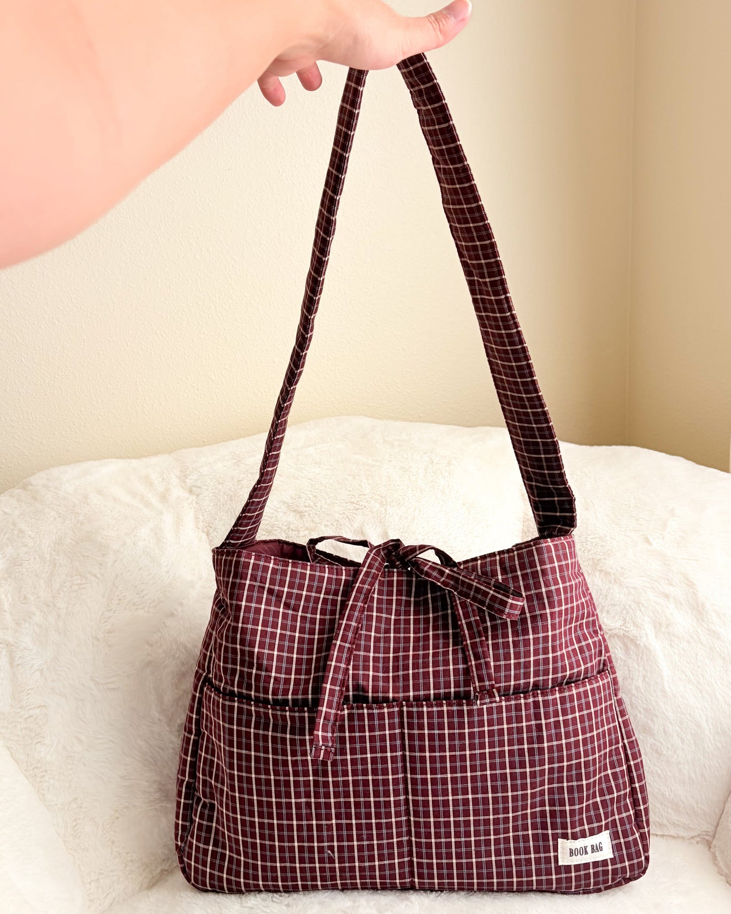 Plaid patterned handbag held by a person on a white surface with a beige background